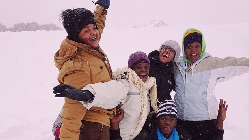 An excited group of young people from refugee backgrounds cheer while it snows at Falls Creek