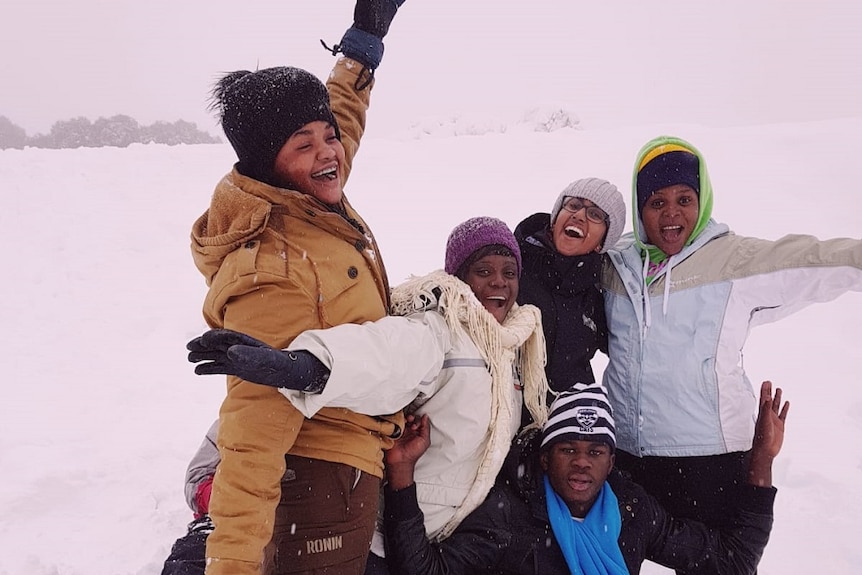 An excited group of young people from refugee backgrounds cheer while it snows at Falls Creek