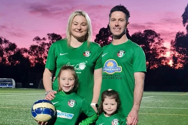 A woman, man, and two young girls, all dressed in green football jerseys smile at the camera.