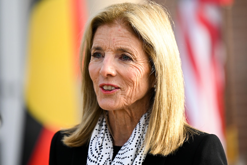 Caroline Kennedy stands in front of flags.