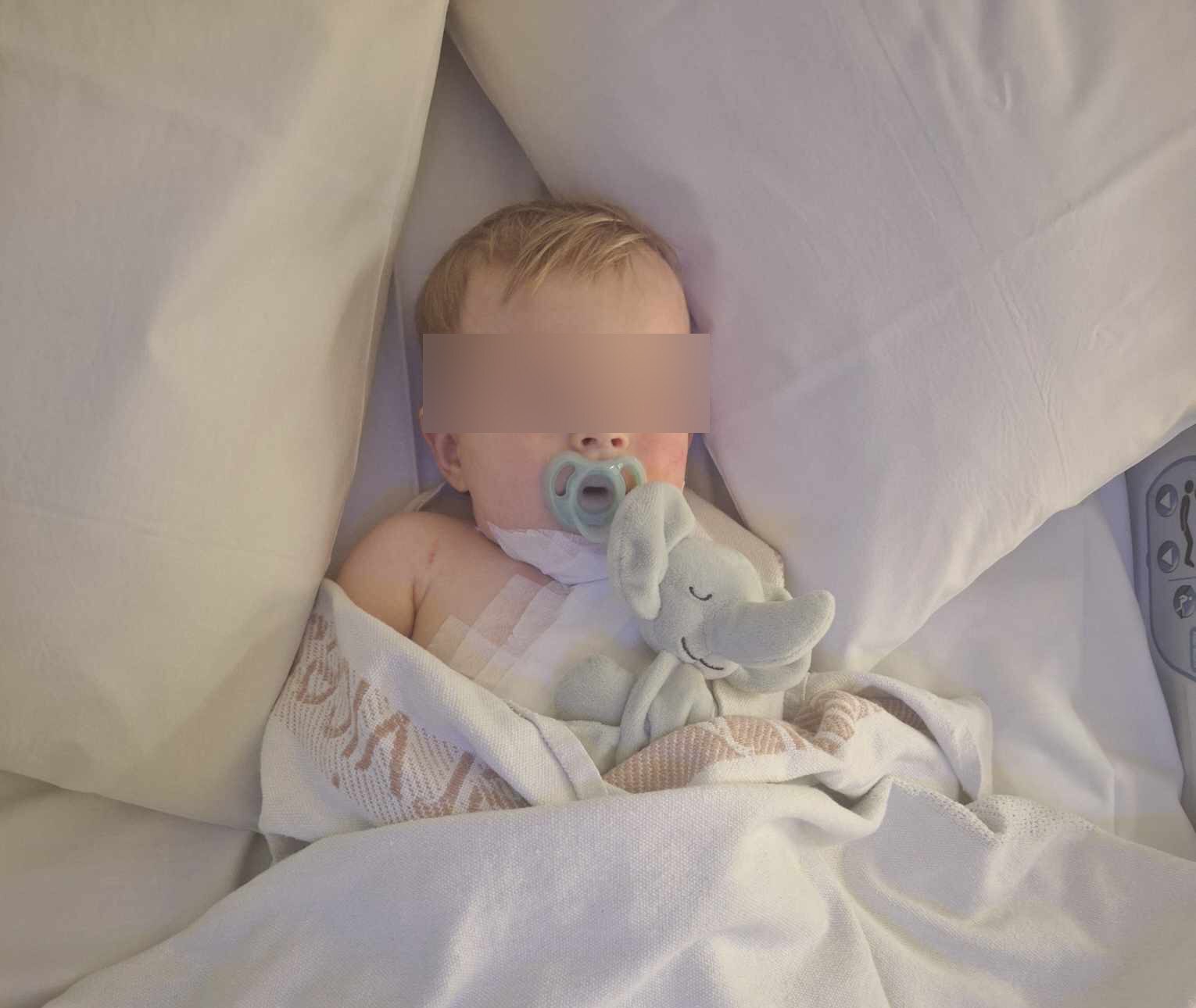 Boy lies in a hospital bed with a pacifier.