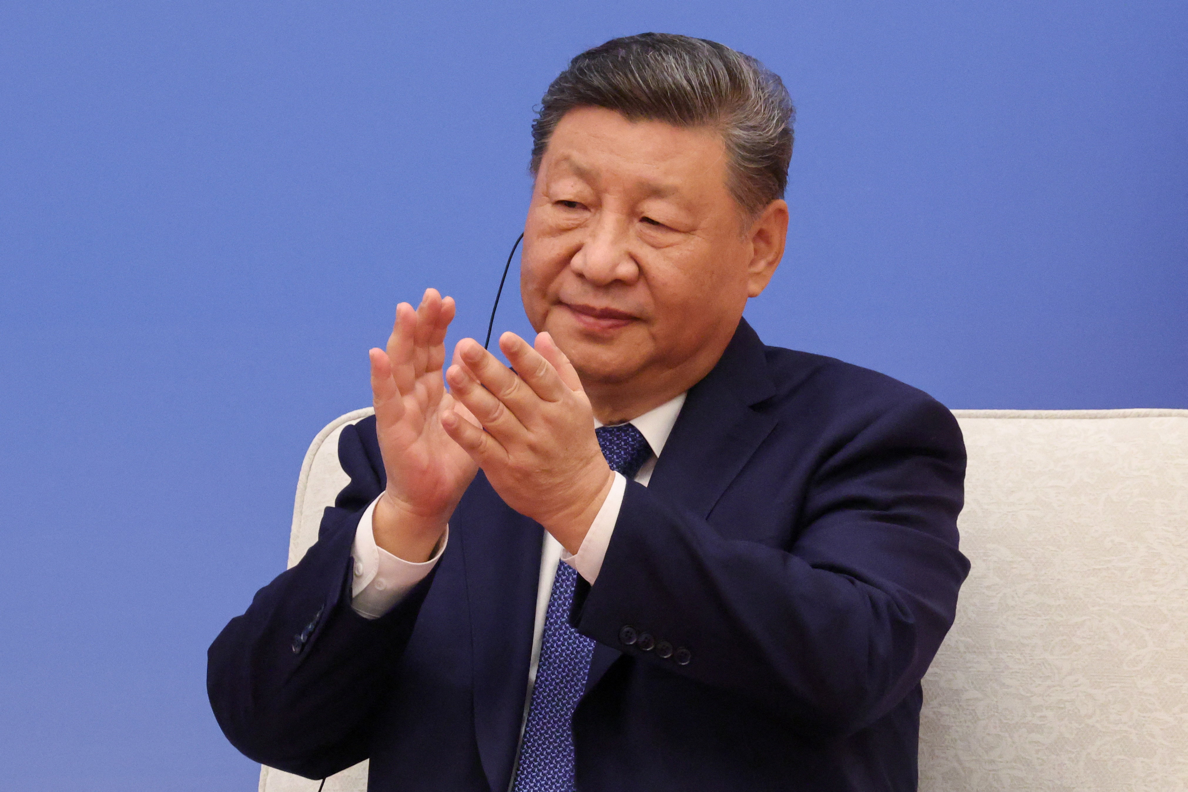 Xi Jinping aplaude sentado con un traje azul oscuro.
