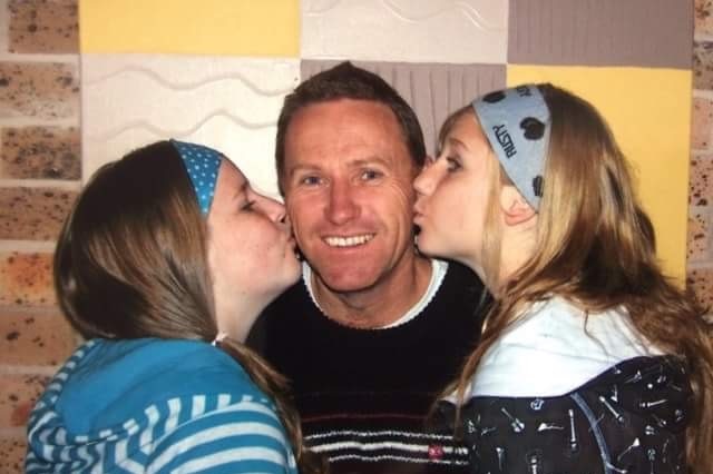 Tony Jenkins between his two daughters, who are kissing him on the cheeks