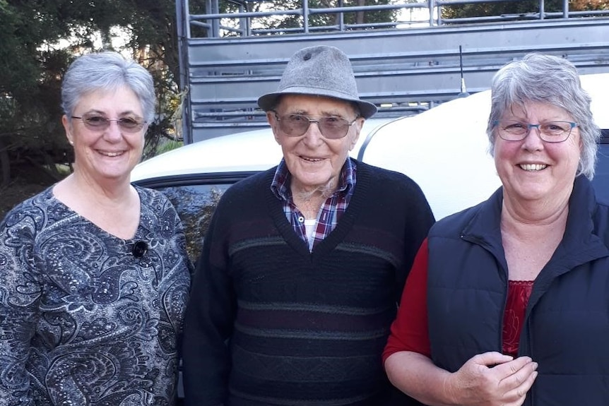 An older man wearing a hat and glasses standing in between two women.