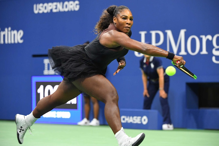 Serena Williams stretches to reach the ball with her racket, intent look of concentration. She wears a black tutu.