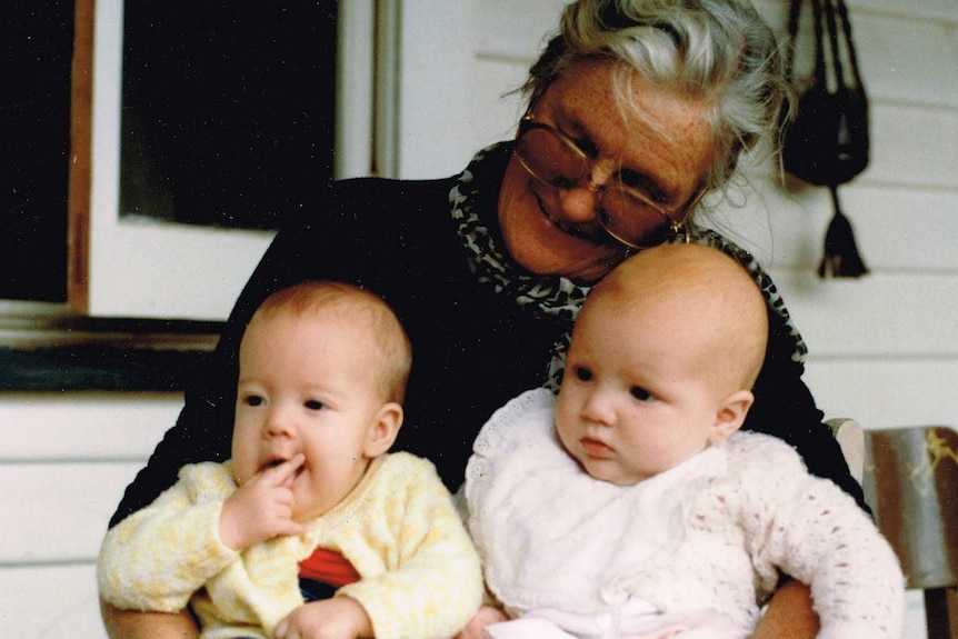 Kathleen Golder sitting down and looking at two babies in her lap.