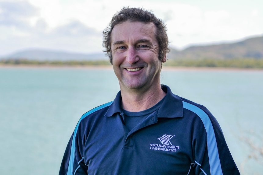 Mike Emslie wearing an Australian Institute of Marine Science T-shirt, and smiling in a portrait taken near the ocean.