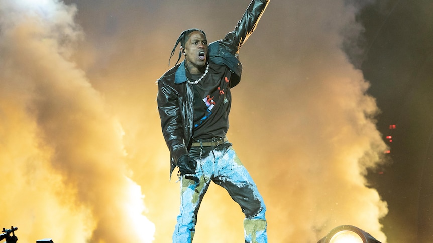 Travis Scott on stage with one arm in the arm in front of stage smoke. 