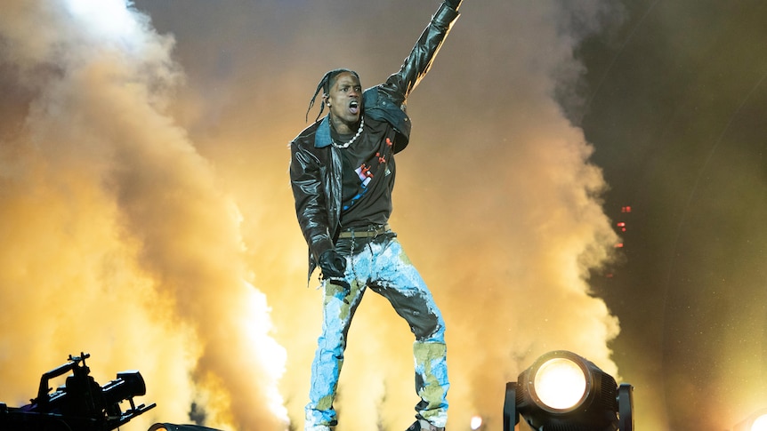 Travis Scott on stage with one arm in the arm in front of stage smoke. 