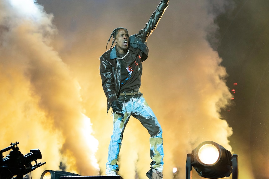 Travis Scott on stage with one arm in the arm in front of stage smoke. 