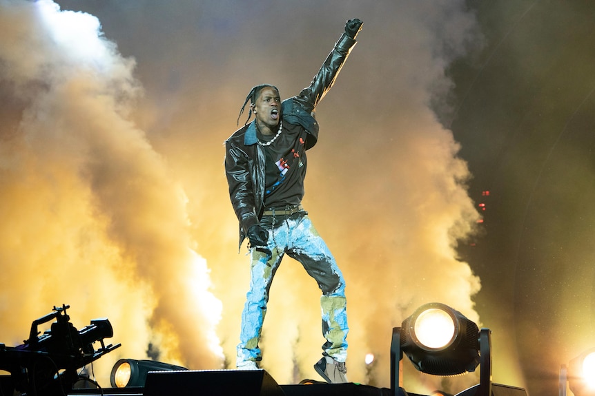 Travis Scott na scenie z ramieniem w ramię przed scenicznym dymem. 