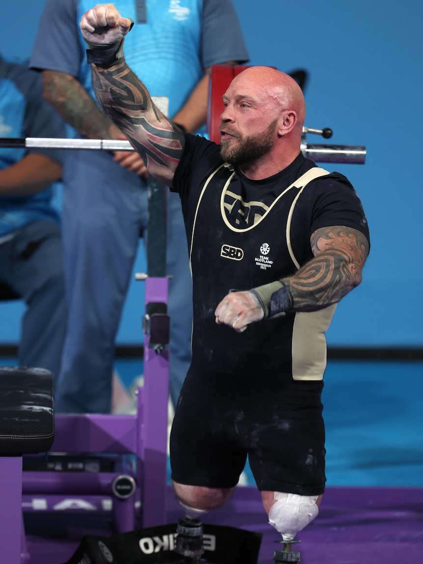 A man wearing black and white punches the air during a weightlifting competition