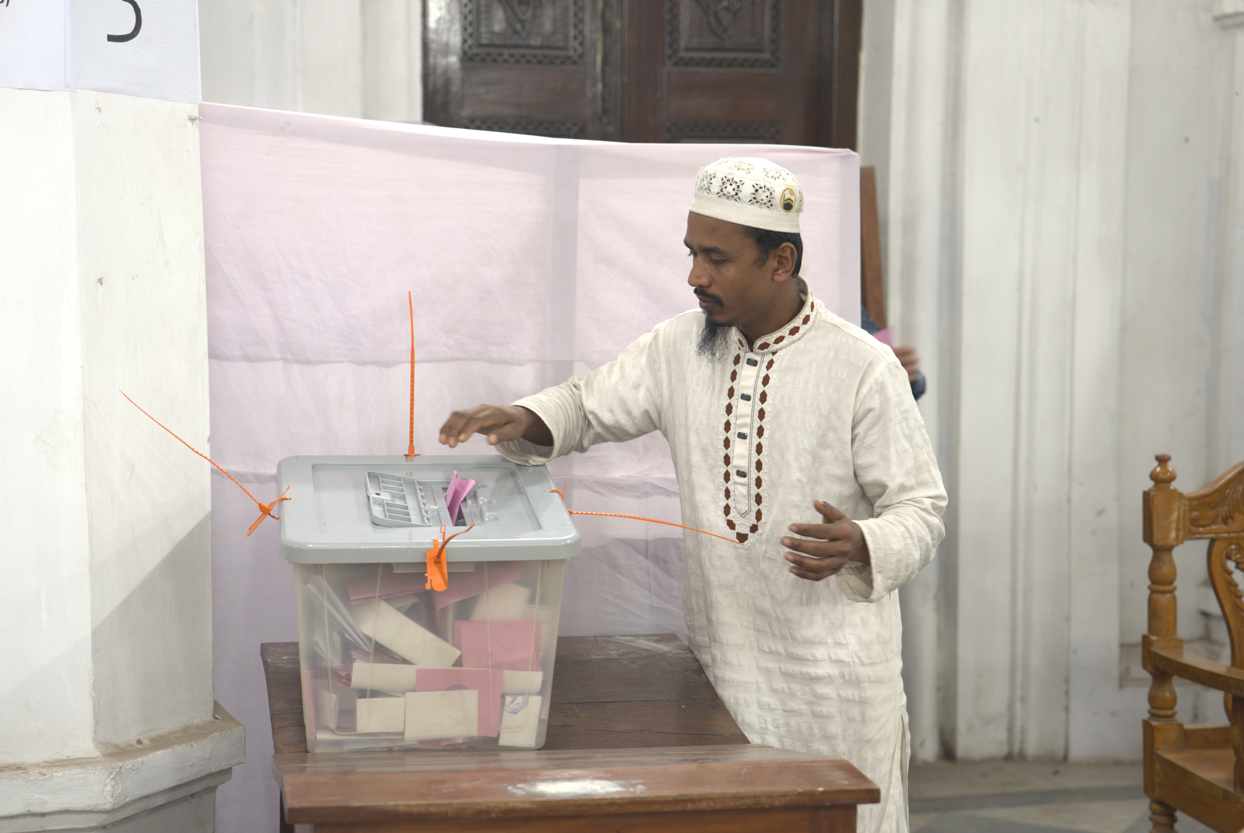 Un hombre emite su voto colocando un trozo de papel rosa en un recipiente de plástico cerrado con bridas de color naranja.