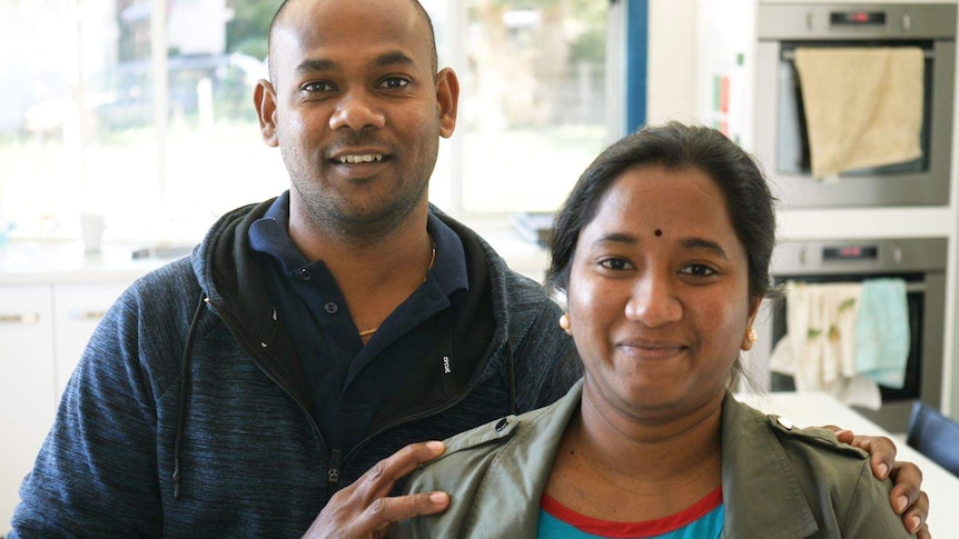 A Tamil couple smiles for the camera, the man with his hands on his wife's shoulders.