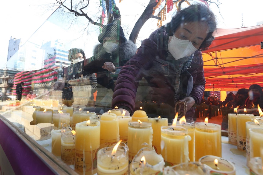 A Korean woman in a face mask lights a candle