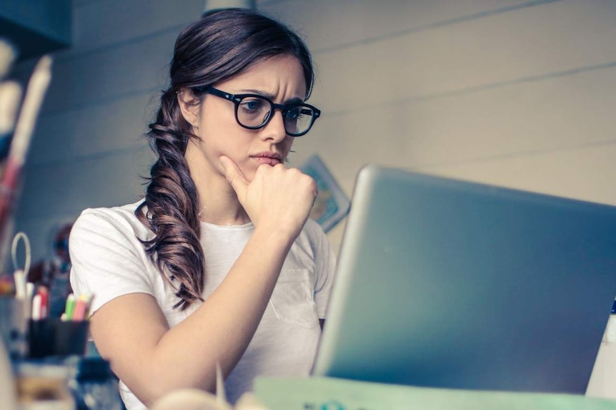 A woman wearing glasses stares at a computer.