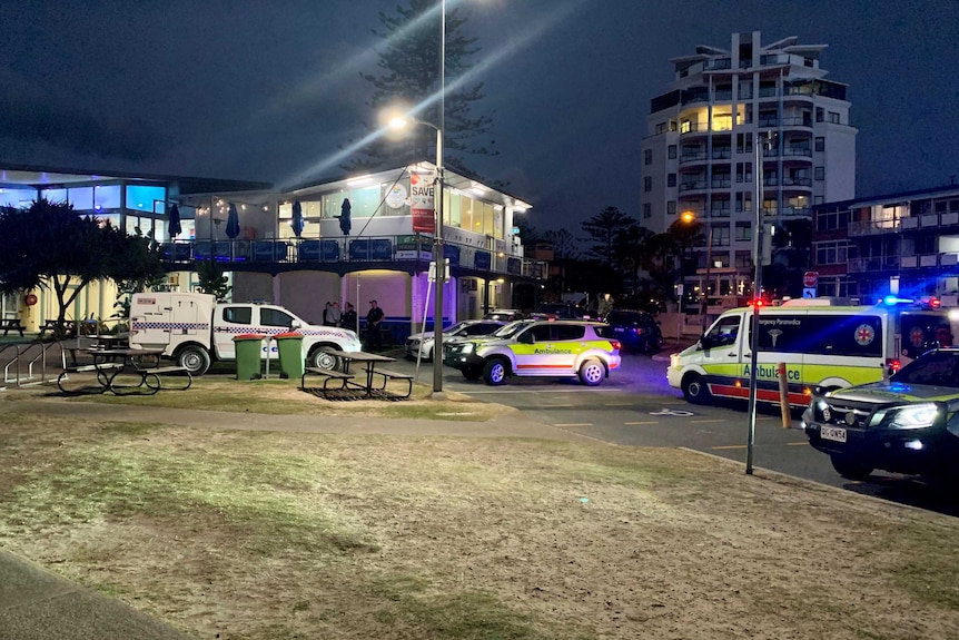 Emergency vehicles are parked at a coastal location at night with tall buildings behind.