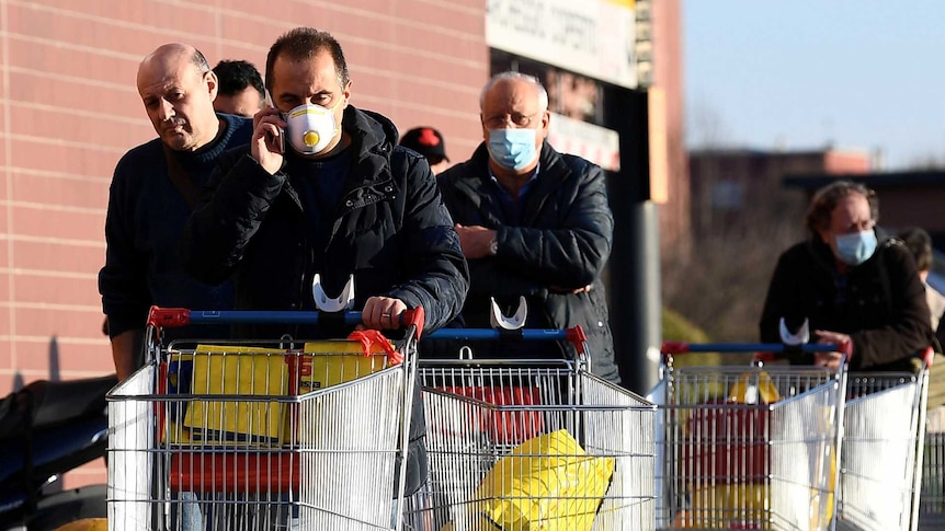 People wearing protective face masks walk towards a supermarket with trolleys