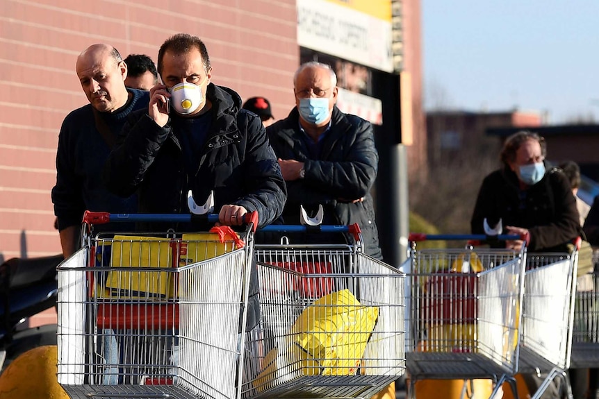 People wearing protective face masks walk towards a supermarket with trolleys
