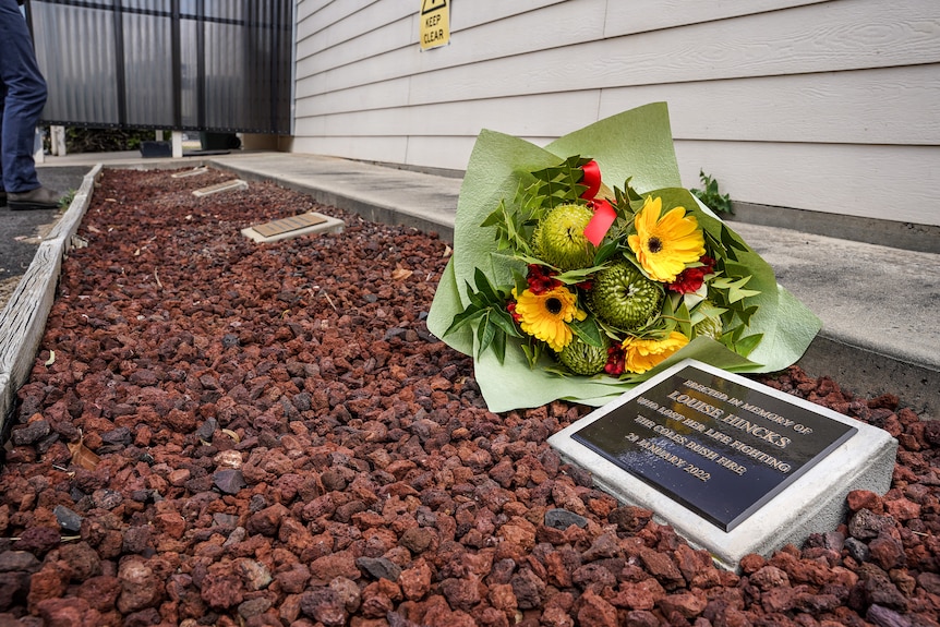 A bunch of flowers sit next to a newly laid plaque atop some pebbles honouring the life of Louise Hincks.