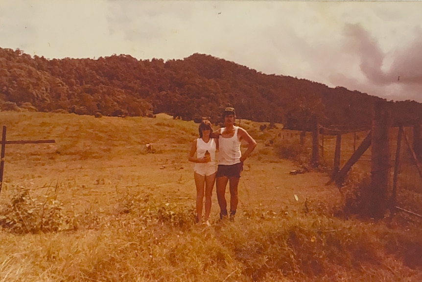 Marg and Alan Ballantyne standing on a large, barren property, mountain terrain is visible in the background 