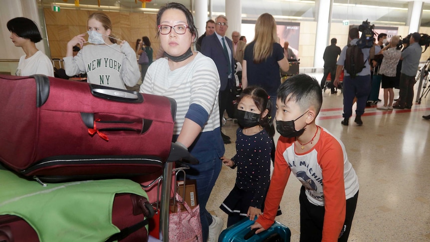 A woman and her children, wearing face masks, arrive at an airport