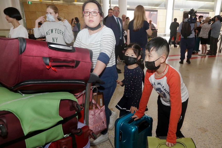 A woman and her children, wearing face masks, arrive at an airport