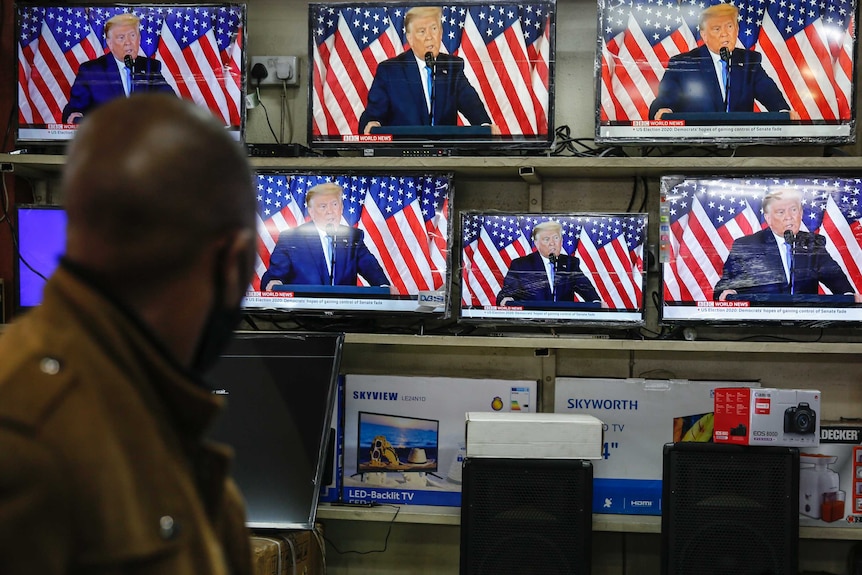 Man watches President Donald Trump on televisions in the window of a shop.