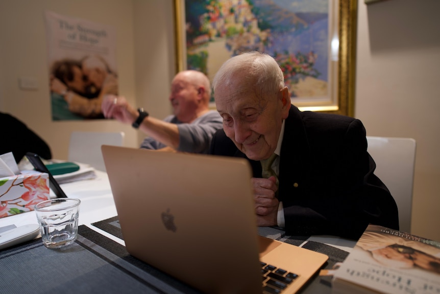 An elderley man smiles at his computer screen.
