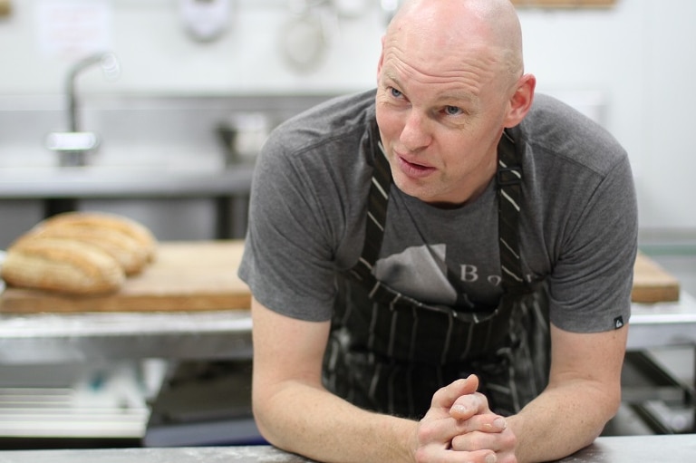 Baker Michael Klausen leaning on a bench in his bakery.