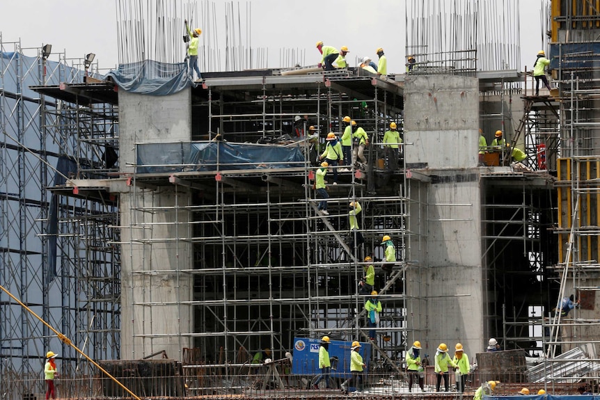 Labourers work at a construction site in downtown Bangkok. They are wearing high visibility clothing and helmets.