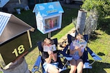 Two kids sitting in camp chairs hold books up to their faces 