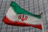 An Iranian flag waves on a flagpole in front of a building.