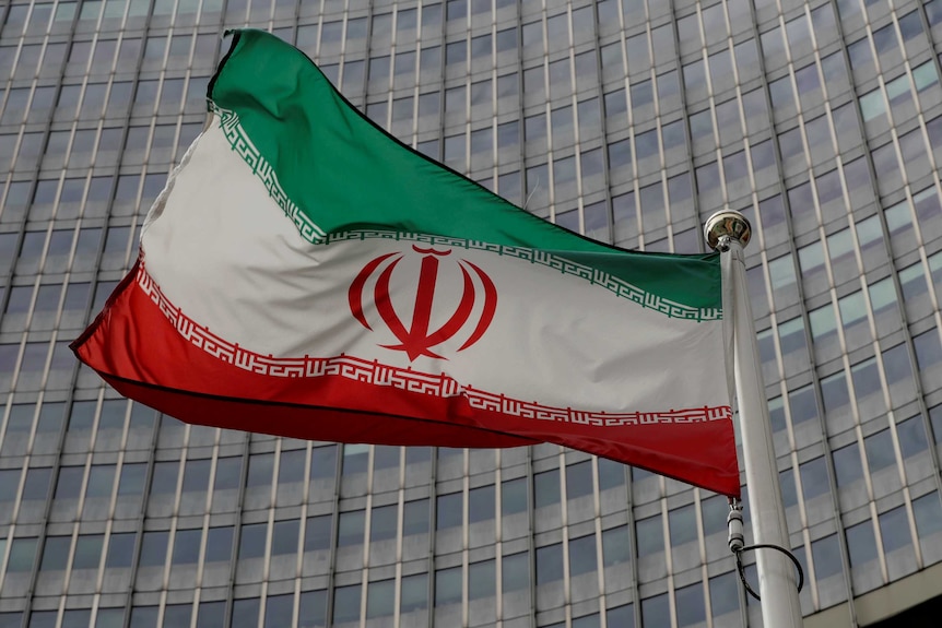 An Iranian flag waves on a flagpole in front of a building.