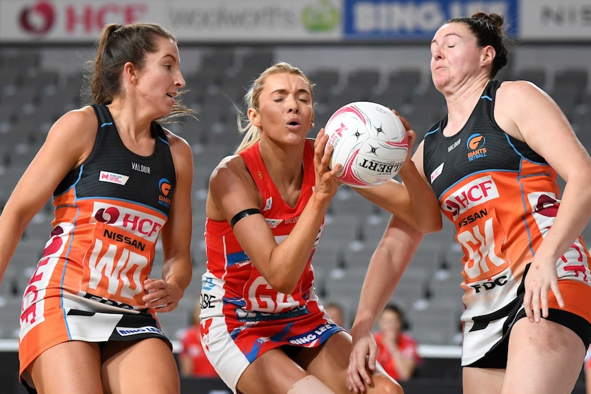 A NSW Swifts Super Netball player holds the ball in two hands as two Giants opponents stand next to her.