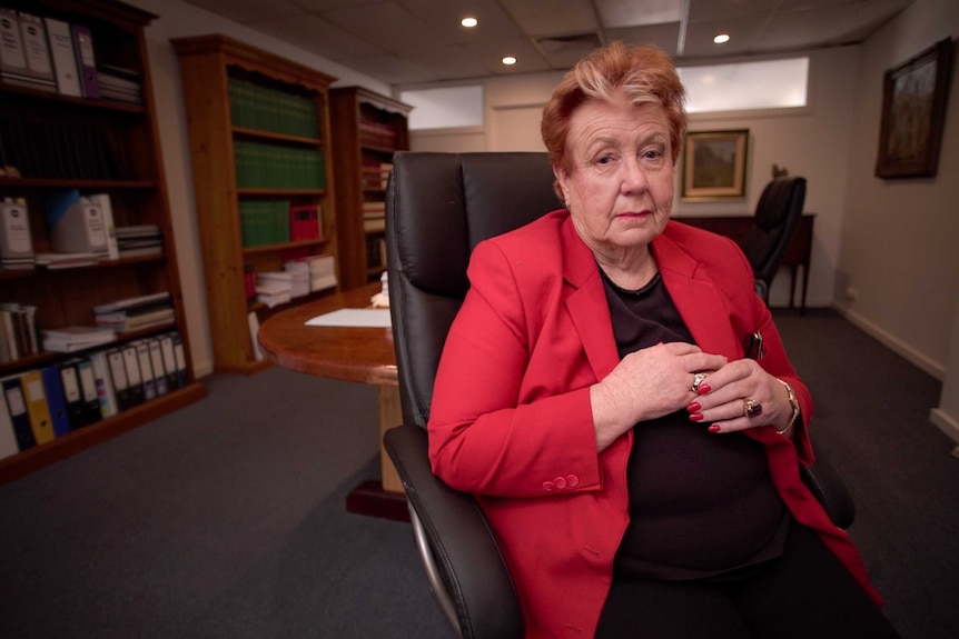 A woman with orange and white hair sits in an office hair in a room with bookcases