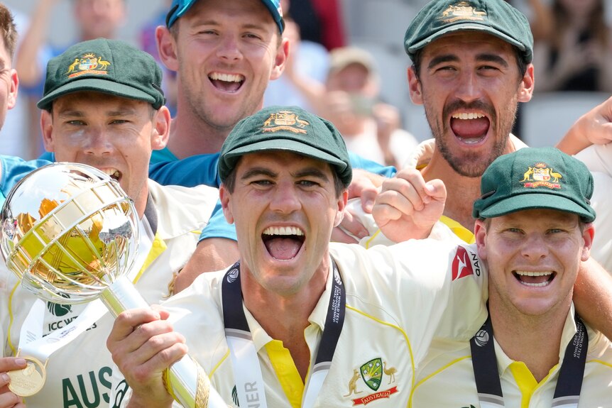 A group of Australian men's cricketers cheer for the camera as the captain holds a large golden mace.