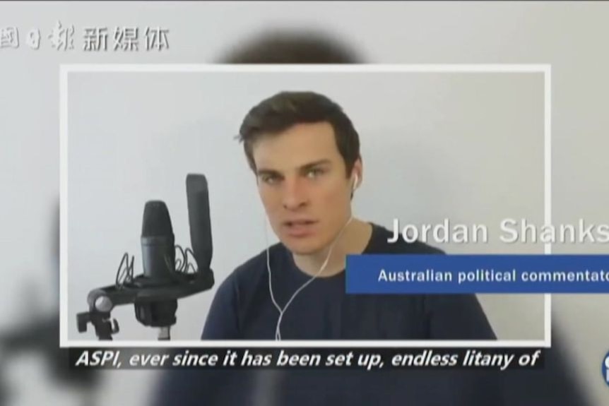 A video still of a white man with brown hair speaking into a microphone in a documentary.