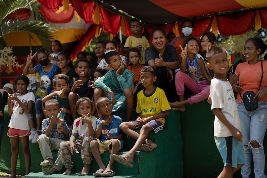 A woman sits with a group of smiling children.