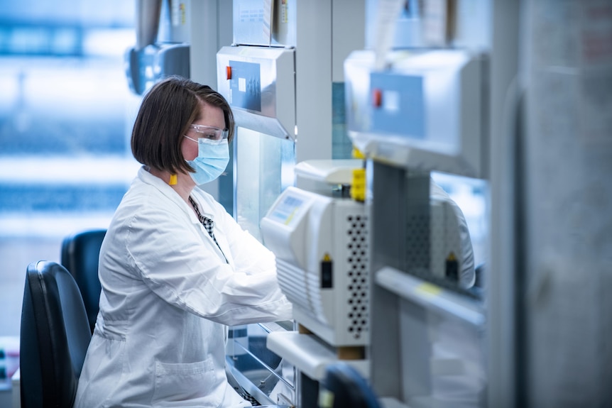 Scientist wearing a mask sits at work bench.