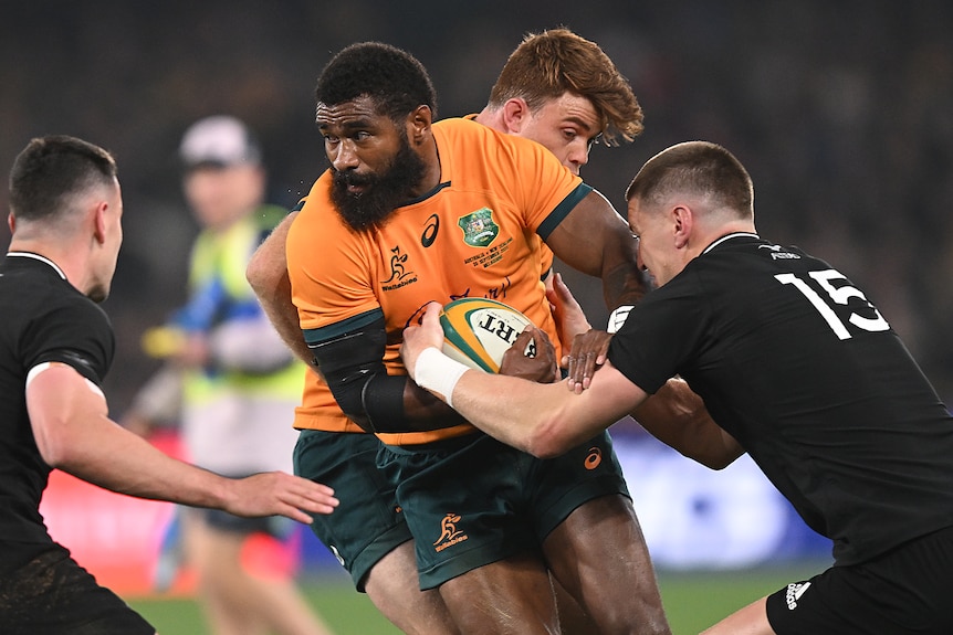 Wallabies winger Marika Koroibete fights off New Zealand All Blacks defenders during a rugby Test.