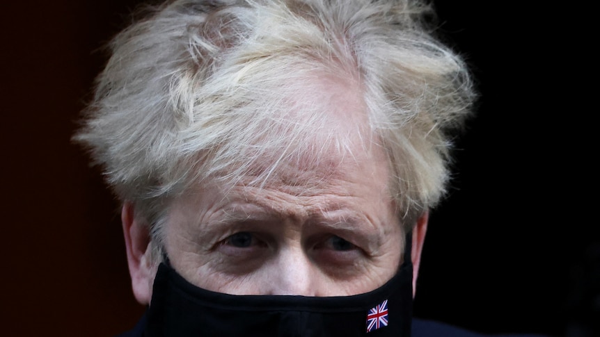 Boris Johnson in a black face mask, with a tiny Union Jack stitched on it 