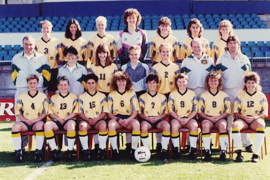 A women's soccer team wearing yellow and white poses for a photo
