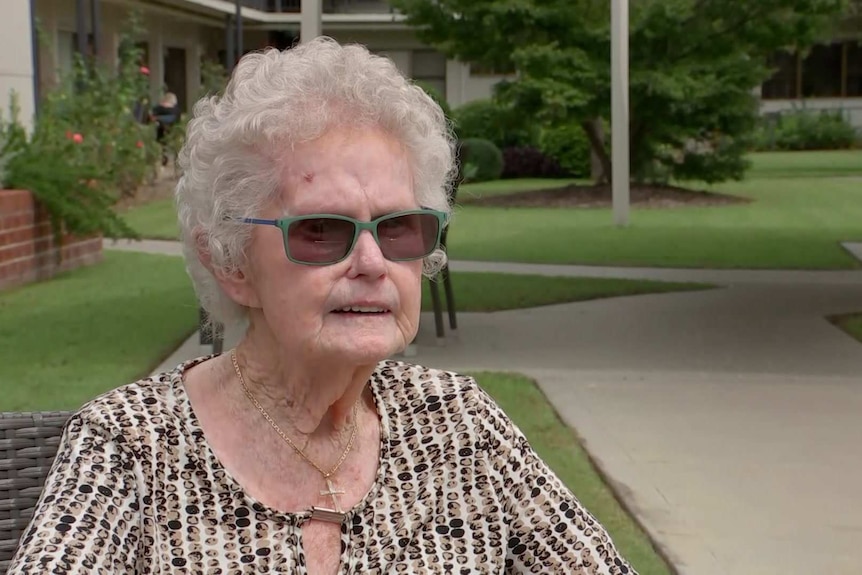 A woman sits on a chair in the courtyard of an aged care home