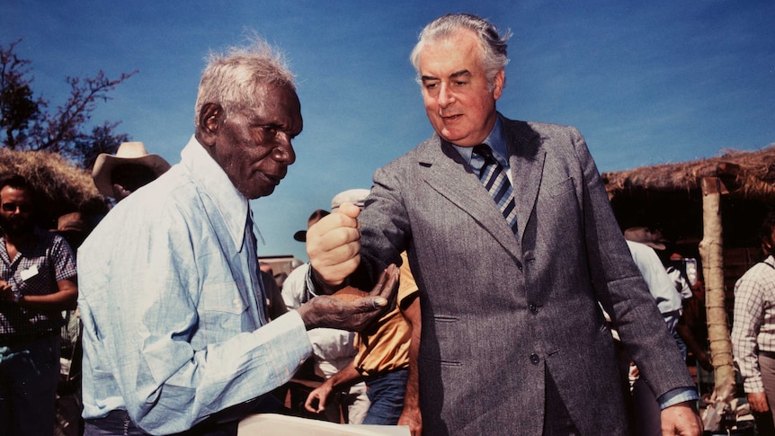 Gough Whitlam puts sand into Vincent Lingiari's hand.