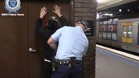 A man holds his arms up against a wall as a policeman search him.