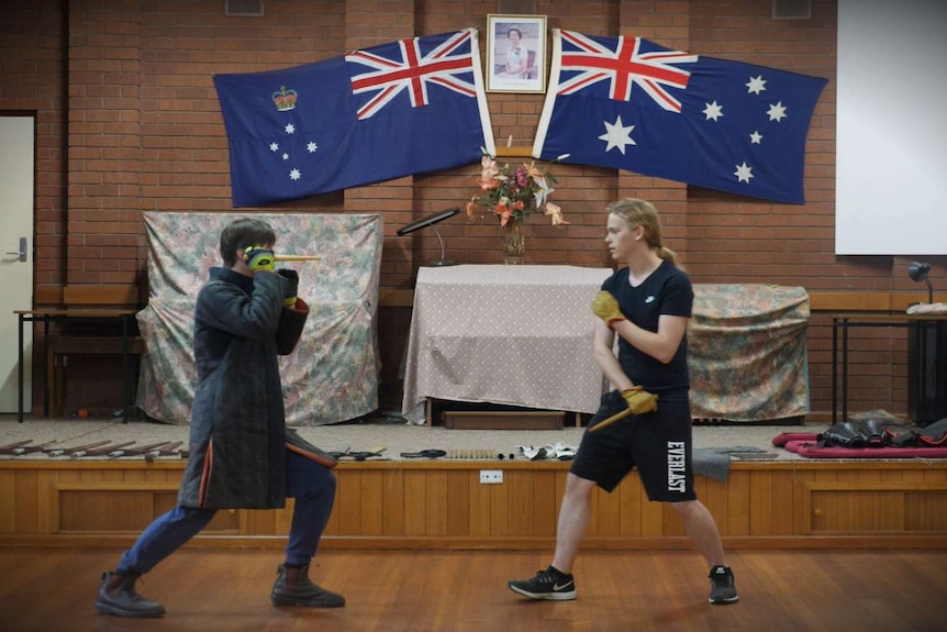 Two young men size each other up, each holds a wooden dagger in his hand.