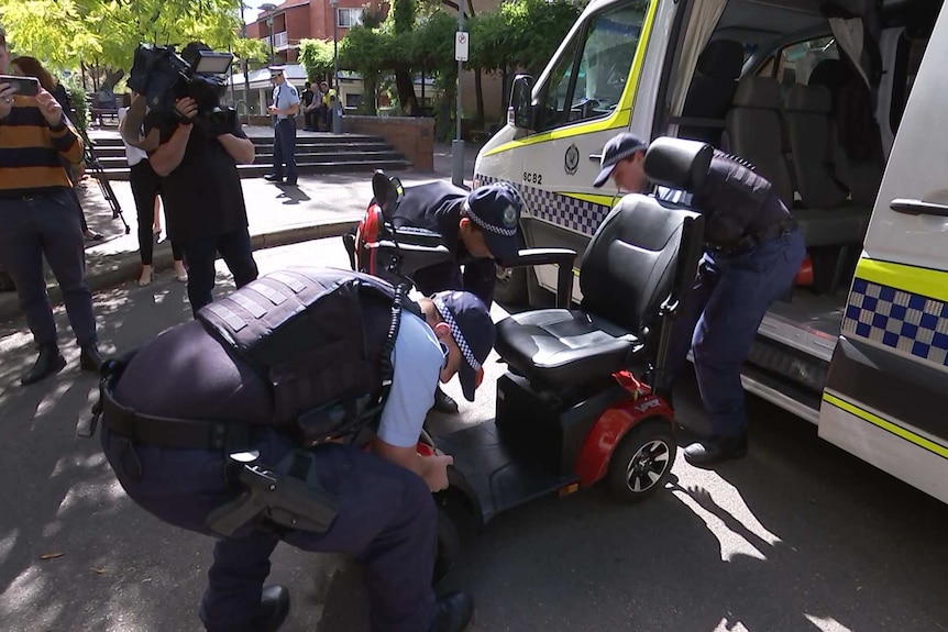 Three police officers getting a mobility scooter out of a police van.