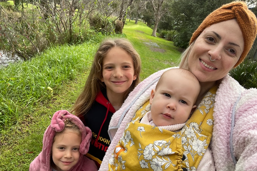 Mum in dressing gown smiles for a selfie with three young girls in a garden.