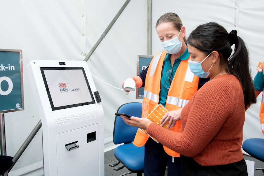 two health workers in masks operating a screen with health information